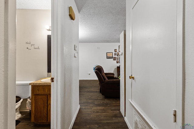 corridor with baseboards, a textured ceiling, dark wood finished floors, and a textured wall