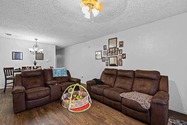 living room featuring wood finished floors, baseboards, visible vents, a textured ceiling, and ceiling fan with notable chandelier