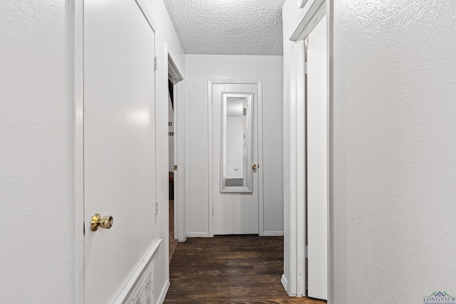 corridor with a textured ceiling, dark wood-style flooring, and a textured wall