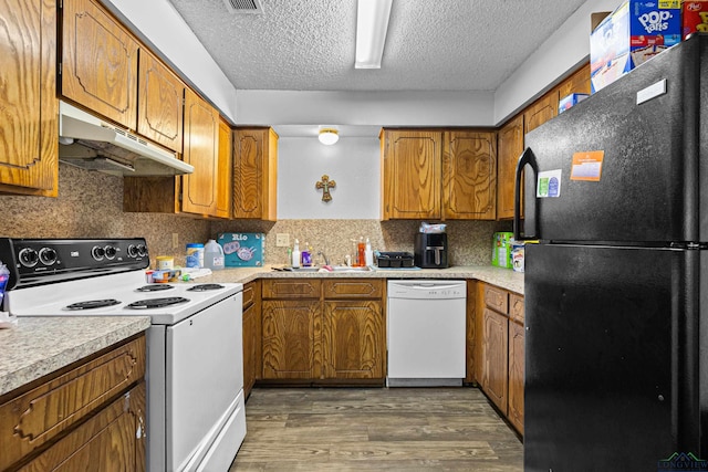 kitchen with under cabinet range hood, a sink, dark wood finished floors, white appliances, and brown cabinetry