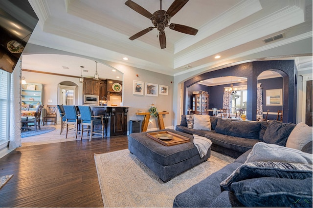 living room with dark hardwood / wood-style floors, ornamental molding, ceiling fan with notable chandelier, and a tray ceiling