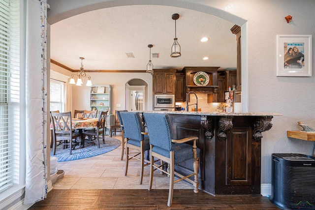 kitchen with stainless steel microwave, a kitchen breakfast bar, ornamental molding, decorative light fixtures, and a chandelier