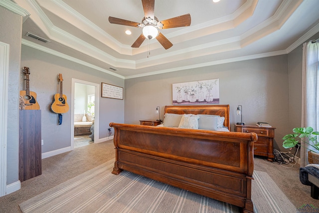 carpeted bedroom with a tray ceiling, ceiling fan, ensuite bathroom, and ornamental molding