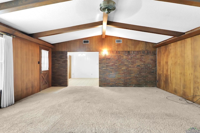 unfurnished living room featuring wooden walls, carpet flooring, visible vents, and vaulted ceiling with beams