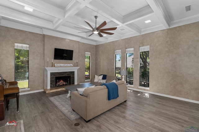 living room with dark wood-type flooring, coffered ceiling, a stone fireplace, ceiling fan, and beamed ceiling