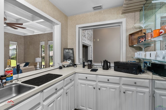 kitchen with coffered ceiling, ceiling fan, sink, beamed ceiling, and white cabinets