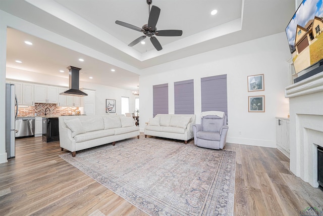 living room featuring ceiling fan, light wood-type flooring, and a tray ceiling