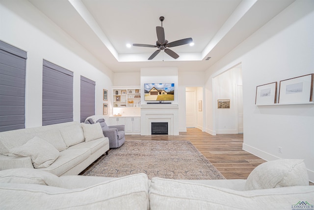 living room featuring a tray ceiling, built in features, ceiling fan, and light hardwood / wood-style floors