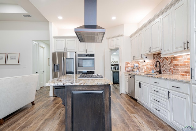 kitchen with backsplash, white cabinets, appliances with stainless steel finishes, a kitchen island, and island exhaust hood