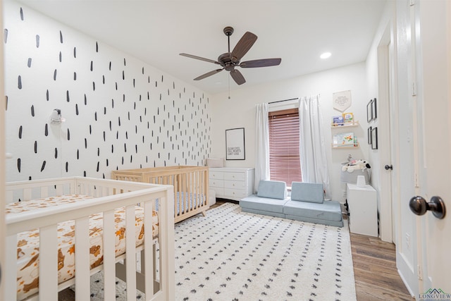 bedroom with hardwood / wood-style flooring, a nursery area, and ceiling fan