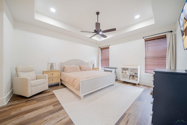 bedroom with hardwood / wood-style flooring, a raised ceiling, and ceiling fan