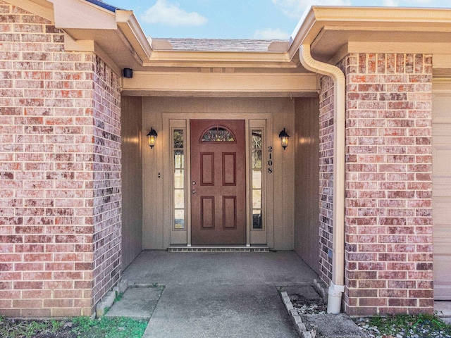 doorway to property with brick siding and a shingled roof