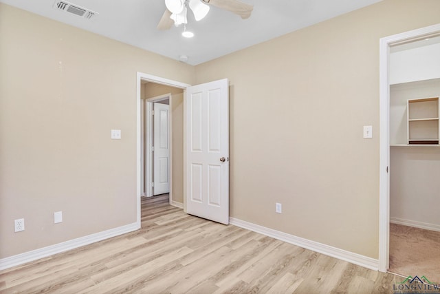 unfurnished bedroom with visible vents, a walk in closet, baseboards, and wood finished floors