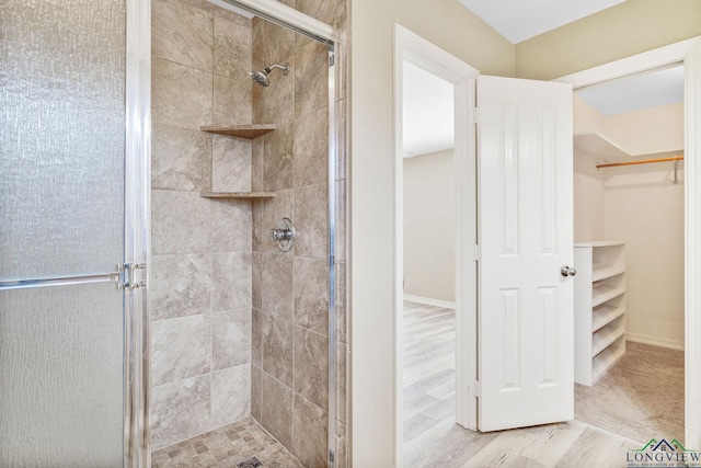 full bath featuring a walk in closet, wood finished floors, and a shower stall