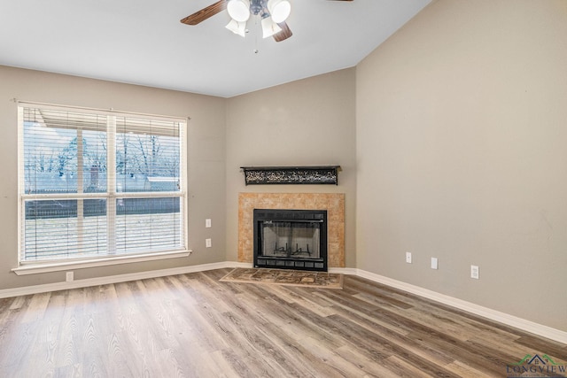 unfurnished living room featuring baseboards, wood finished floors, ceiling fan, and a tile fireplace