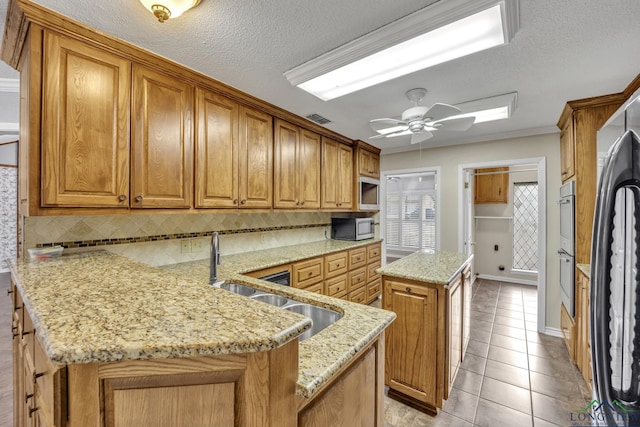kitchen with decorative backsplash, a peninsula, a center island, brown cabinets, and light stone counters