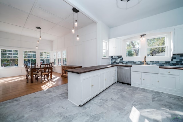 kitchen with kitchen peninsula, hanging light fixtures, stainless steel dishwasher, white cabinets, and sink