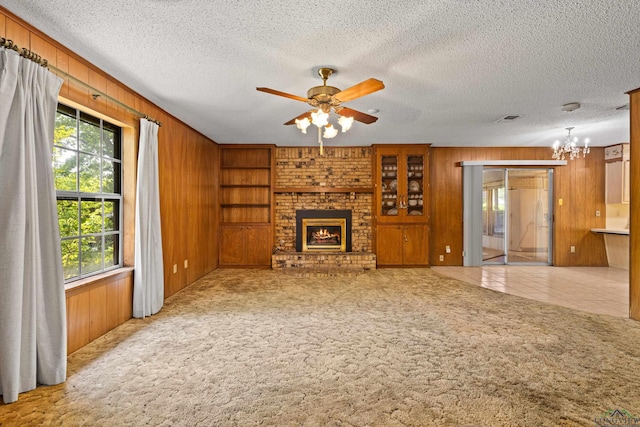 unfurnished living room featuring carpet, wooden walls, a textured ceiling, and a brick fireplace