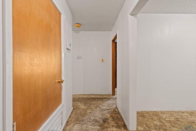 corridor with a textured ceiling, carpet flooring, and baseboards