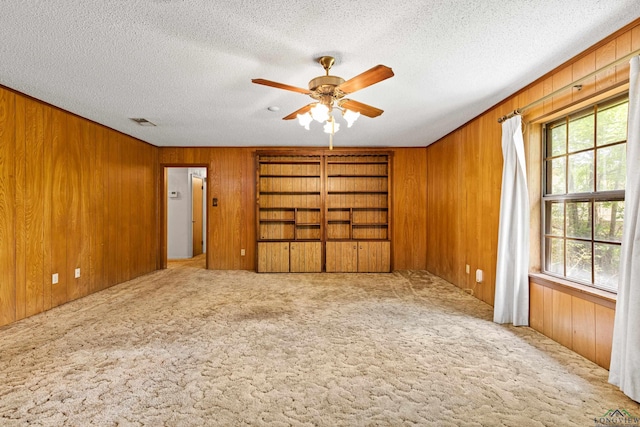 carpeted spare room with a textured ceiling, wooden walls, a ceiling fan, and visible vents