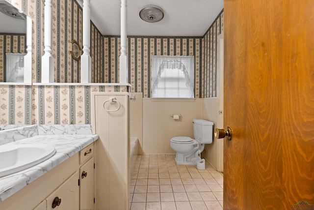 full bath featuring tile patterned floors, wallpapered walls, toilet, vanity, and a textured ceiling