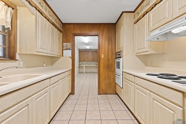 kitchen with under cabinet range hood, light tile patterned floors, white appliances, wood walls, and light countertops