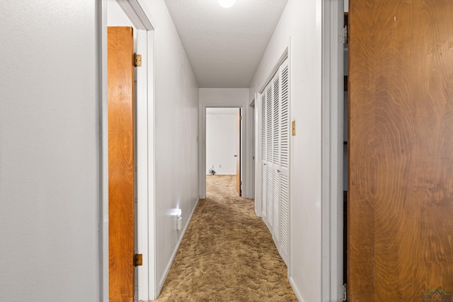 corridor with a textured ceiling, carpet flooring, and baseboards