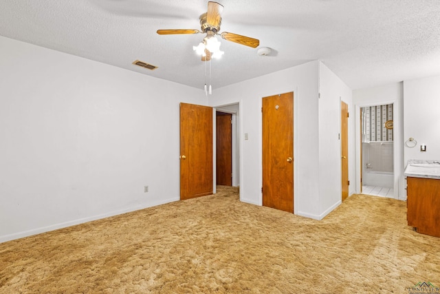 unfurnished bedroom with a textured ceiling, carpet flooring, visible vents, ensuite bathroom, and baseboards
