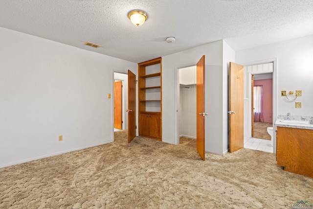 unfurnished bedroom featuring light carpet, a sink, baseboards, visible vents, and a textured ceiling