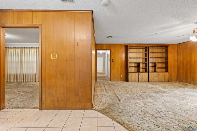 empty room featuring light colored carpet, a textured ceiling, a ceiling fan, wooden walls, and light tile patterned flooring