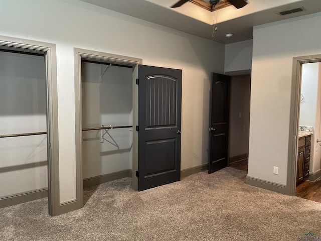 unfurnished bedroom with ensuite bath, ceiling fan, and dark carpet