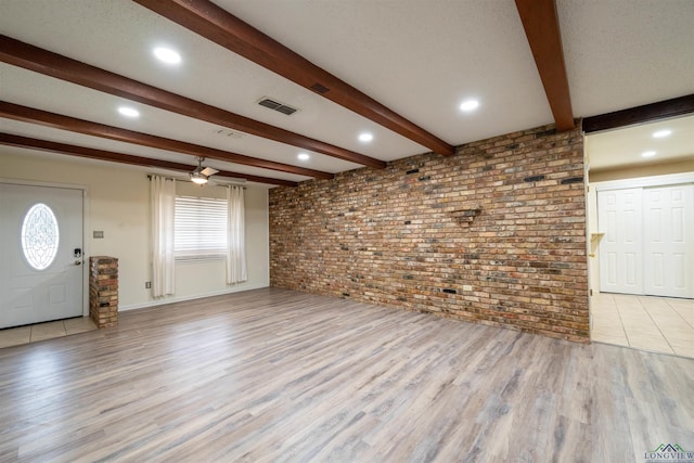 unfurnished living room with a textured ceiling, brick wall, visible vents, light wood-style floors, and beam ceiling