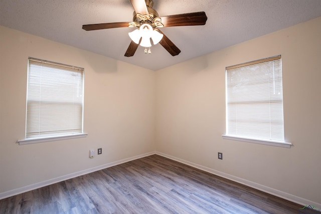 spare room with a textured ceiling, wood finished floors, a wealth of natural light, and baseboards