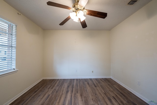 spare room with dark wood-type flooring, visible vents, ceiling fan, and baseboards