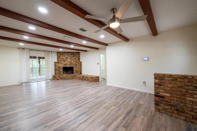 unfurnished living room with visible vents, wood finished floors, beamed ceiling, a textured ceiling, and a fireplace