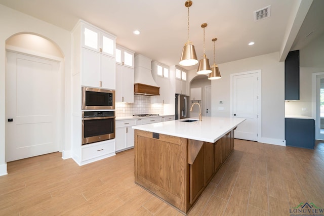 kitchen featuring a large island with sink, stainless steel appliances, visible vents, tasteful backsplash, and custom range hood