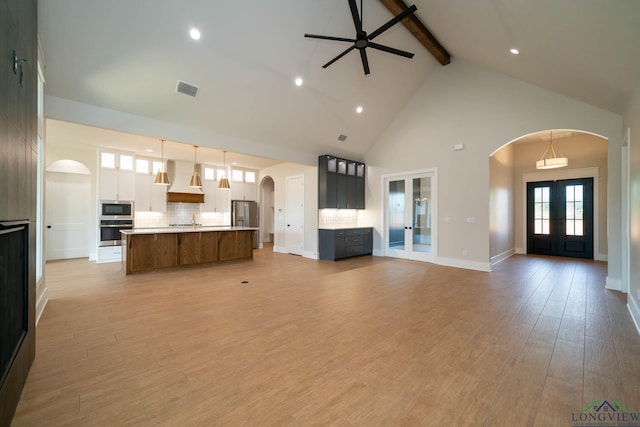 unfurnished living room featuring french doors, arched walkways, visible vents, beamed ceiling, and high vaulted ceiling