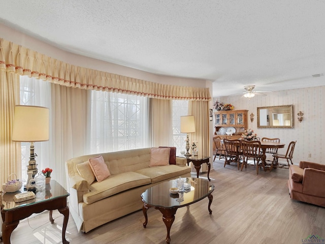 living area with a wealth of natural light, a textured ceiling, light wood-style flooring, and a ceiling fan