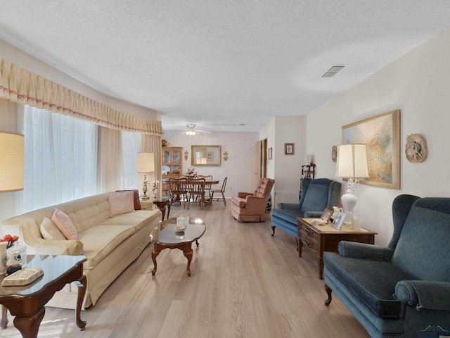 living room with visible vents, a textured ceiling, ceiling fan, and light wood finished floors