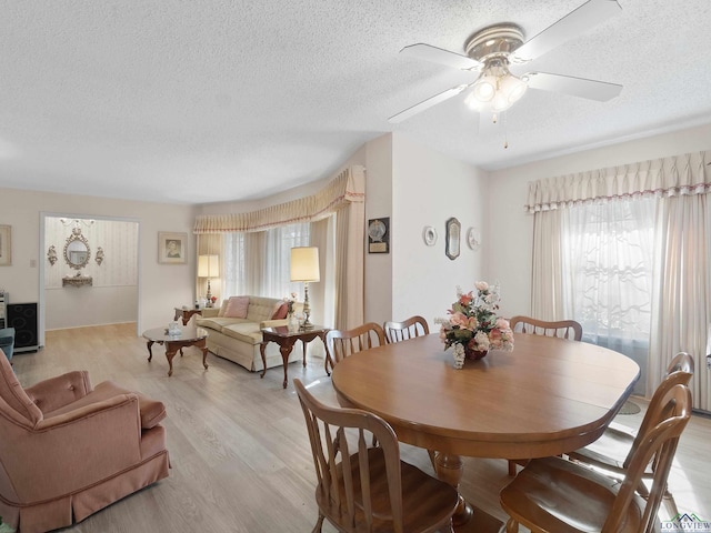 dining area with light wood-style floors, a ceiling fan, and a textured ceiling