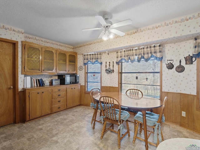 dining space with a wainscoted wall, wood walls, a textured ceiling, and wallpapered walls