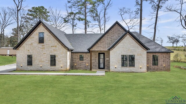 french country home with a shingled roof, a front yard, and brick siding