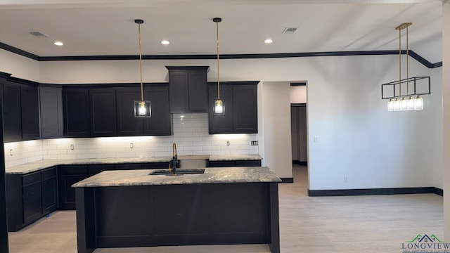 kitchen with light stone counters, a center island with sink, and pendant lighting