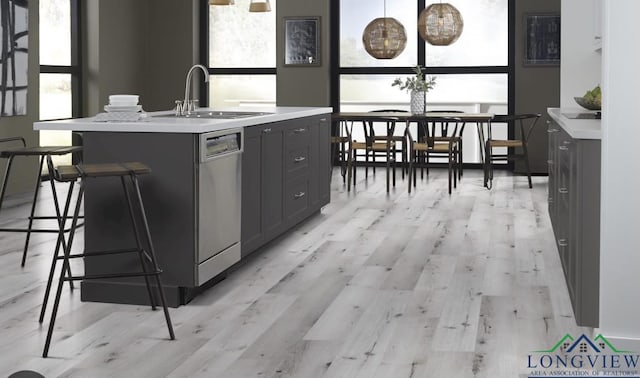 kitchen featuring stainless steel dishwasher, a kitchen island with sink, sink, pendant lighting, and gray cabinets