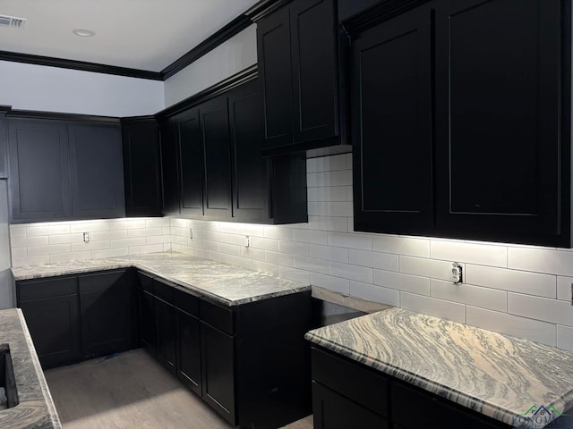 kitchen featuring crown molding, light hardwood / wood-style floors, light stone counters, and backsplash