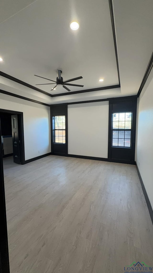 empty room featuring a raised ceiling, ceiling fan, crown molding, and light wood-type flooring