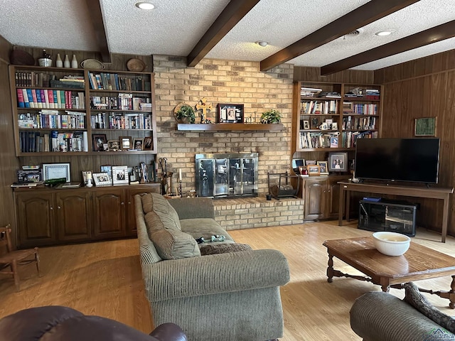 living room with beam ceiling, light hardwood / wood-style flooring, a textured ceiling, wooden walls, and a fireplace