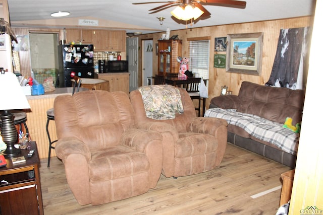 living area featuring wooden walls, vaulted ceiling, light wood-style flooring, and ceiling fan