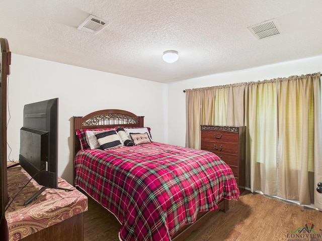 bedroom with visible vents, a textured ceiling, and wood finished floors
