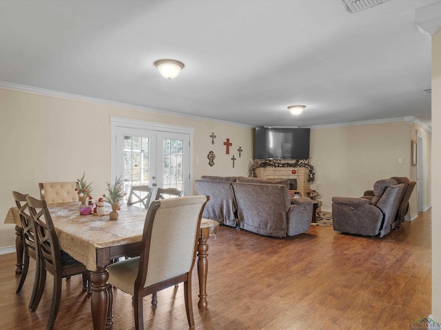 dining area featuring hardwood / wood-style floors, french doors, crown molding, and a brick fireplace